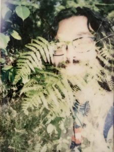 Image of white male face iwth dark hair and beard blended with ferns