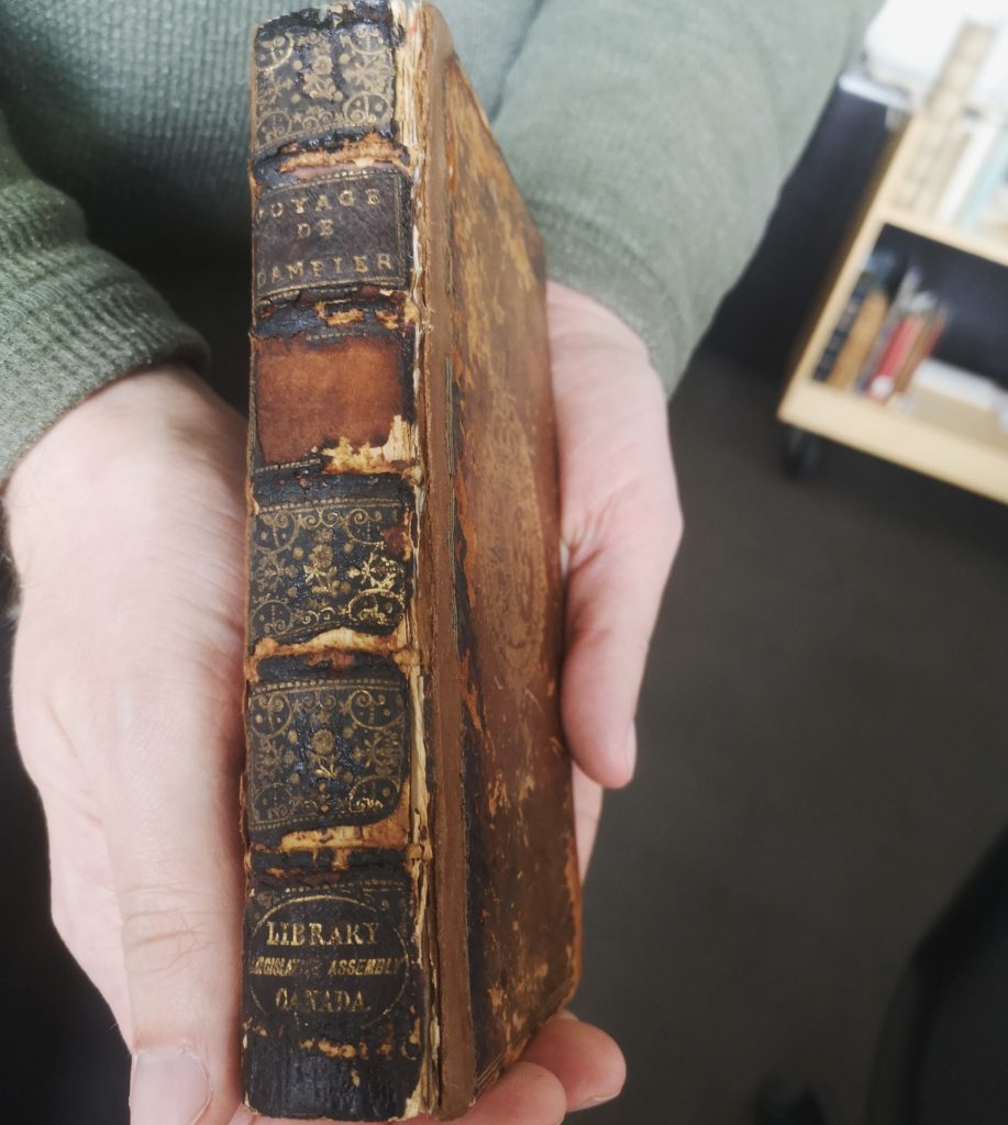 Hands hold charred copy of the "Voyages de Dampier" with binding side up