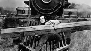 Buster Keaton on the cowcatcher of a train engine, holding a large piece of lumber