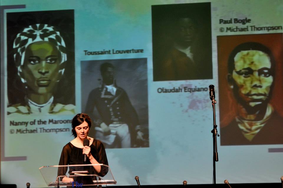 Photo of Nicola Abram onstage in front of Prezi presentation.