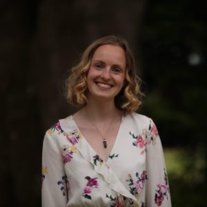 A blonde woman in a white flowery top, smiling