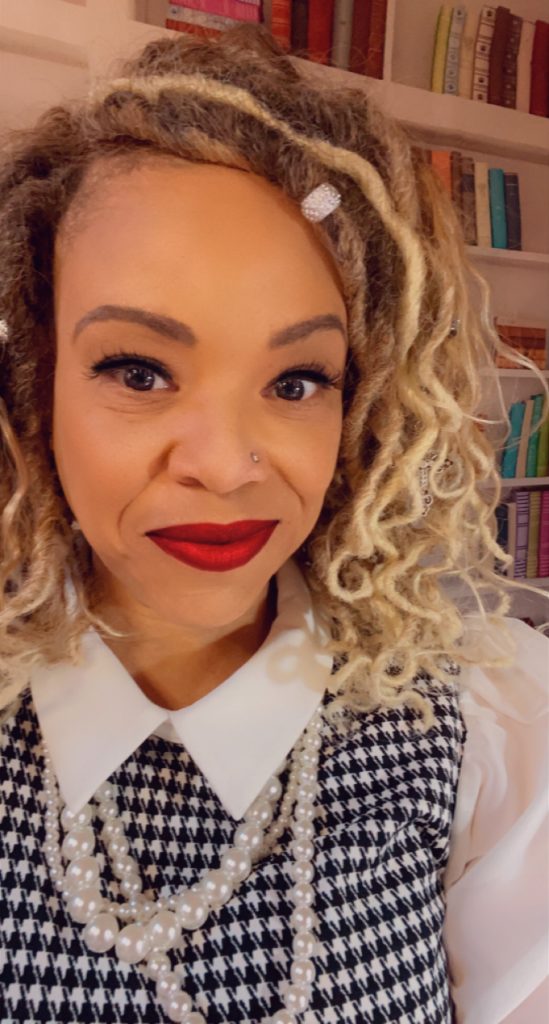 Professor Deborah Elizabeth Whaley smiles at the camera. She is wearing a white shirt with a blue and white patterned vest.