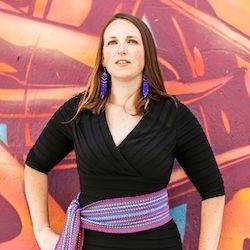 Elizabeth LaPensee, Assistant Professor of Media and Information at Michigan State University, stands in front of a painted mural, hand on hip, and looks stoically at the camera.