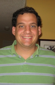 Eric Berlatsky smiles at the camera with short brown hair and is wearing a green and white striped polo.