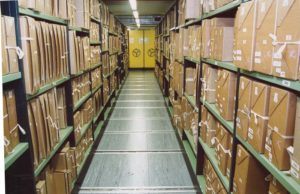 An archive with shelves of records housed in protective cases lining the walls
