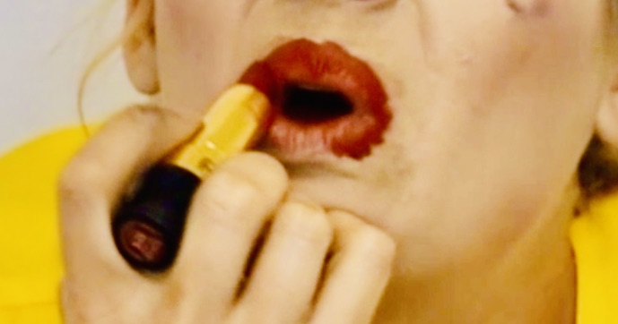 Image shows a person applying red lipstick outside the boundaries of their lips