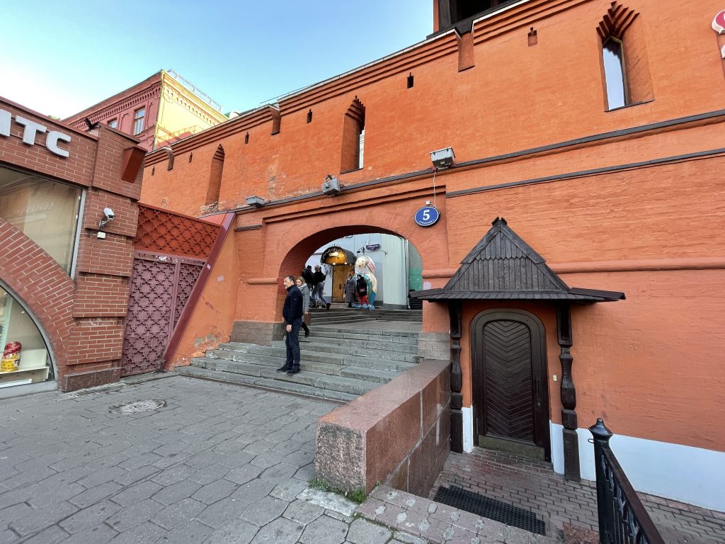 A medieval red brick wall is integrated into the current city. People stroll through an archway that probably used to have some gates. 