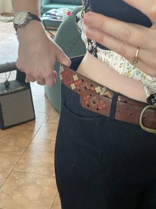 The image shows a woman’s torso from mid thigh to bust, partially blocked by the hand and phone taking the picture. Her other thumb is Hoboken into her waistband, pulling it to the side to show the 2 extra inches of air between her trousers and her body.