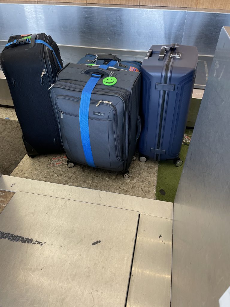 Four very large suitcases are lined up waiting to go on the airline's conveyor belt into the checked baggage system.