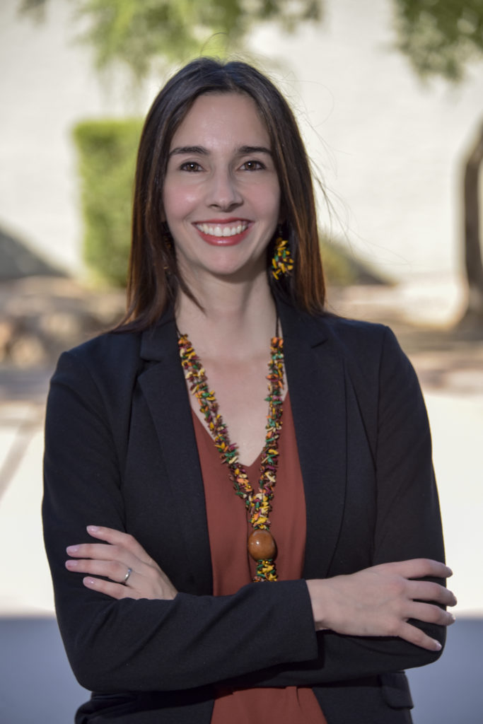 STEM Ed PaCER Fellow Dr. Carolina Michel. Long brown hair, wide smile, big multicolored earrings and matching necklace, red-brown shirt, black jacket,